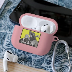 Könnte beinhalten: Rosa AirPods Pro Hülle mit silbernem Karabinerhaken. Die Hülle hat ein gelbes Quadrat mit einer schwarz-weißen Anime-Illustration von drei Charakteren. Weiße AirPods befinden sich im geöffneten Gehäuse.