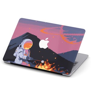 May include: A laptop with a pixelated design featuring an astronaut roasting marshmallows over a campfire in a pink and blue landscape. The laptop has an Apple logo on the lid.