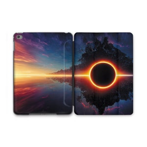 Könnte beinhalten: Eine schwarze iPad-Hülle mit einem farbenfrohen Sonnenuntergang und einem schwarzen Kreis mit einem leuchtend orangen Ring darum. Das Bild spiegelt sich im Wasser darunter wider.