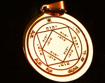 Puede incluir: Un colgante circular de metal dorado con un diseño geométrico grabado que incluye un cuadrado central y un patrón de estrella. La superficie está inscrita con caracteres y símbolos hebreos, incluido un pequeño asterisco en la parte superior.