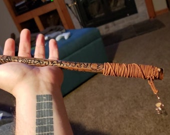 May include: A handcrafted wooden wand with a clear crystal tip and copper wire accents. The wand features etched symbols and is wrapped with brown twine. A small leather cord with a few beads hangs from the end.