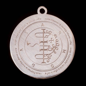 May include: A silver-colored, circular pendant with a loop at the top. The pendant features engraved symbols and text, including the words "Ayer avage Aloren Asmoday aken." The design is centered on the pendant.