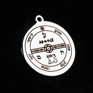 May include: A circular silver-toned metal pendant featuring an engraved design with a central six-pointed star, various geometric symbols, and Hebrew characters arranged in a circular border. The pendant includes a small loop at the top for attachment.