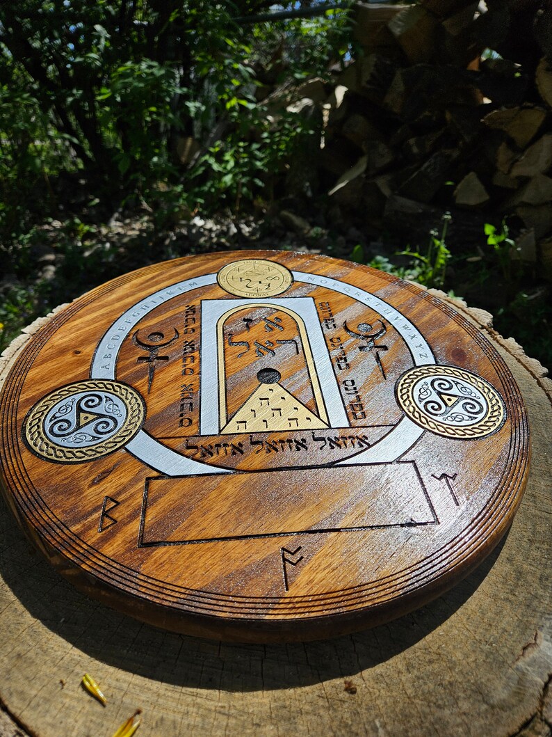 May include: A wooden round disc with a silver and gold design. The design features a circle with a triangle inside, a square with a circle inside, and a rectangle with a circle inside. The disc also has a blank rectangle in the center. The disc is surrounded by a circle of text in a foreign language.