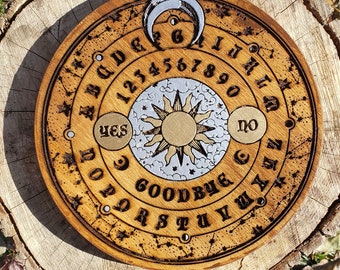 May include: A wooden Ouija board with a sun and moon design. The board features the alphabet, numbers 1-9 and 0, and the words "yes", "no", and "goodbye".