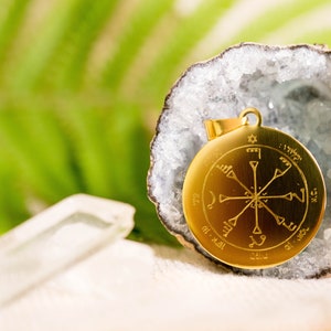 Op de afbeelding: Een gouden hanger met een ster van David en Arabische tekst op een witte achtergrond. De hanger bevindt zich in een kristallen geode.