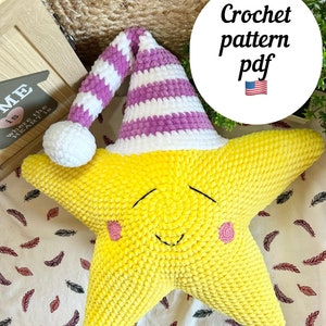 May include: A yellow star-shaped crochet pillow with a smiling face and pink cheeks. It wears a white and purple striped hat with a white pom-pom. The image includes the text "Crochet pattern pdf".