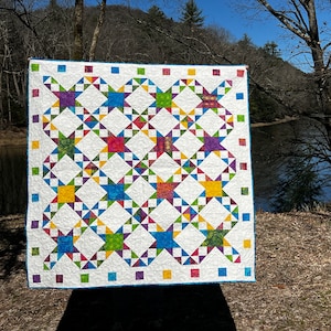 Pode incluir: Um edredom branco com um design de patchwork que apresenta uma variedade de cores, incluindo azul, verde, amarelo, vermelho e roxo. O edredom é feito de quadrados e triângulos, e o design lembra um padrão de estrela.