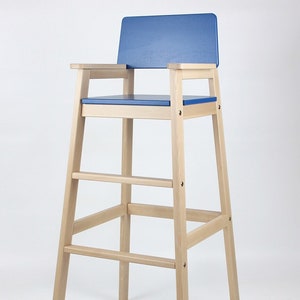Peut inclure: Chaise de bar haute en bois avec assise et dossier bleus. La chaise est dotée d'accoudoirs et de repose-pieds, fabriquée en bois clair. Le design est simple et moderne, adapté à une cuisine ou un bar. La hauteur de la chaise est d'environ 100 cm.