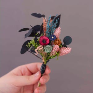 Boutonniere invernale con eucalipto blu conservato, fiori secchi e fiori di carta in rosa antico, bordeaux e blu navy