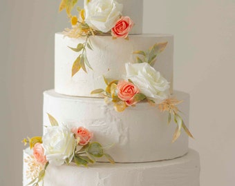 May include: A four-tier white wedding cake decorated with delicate peach and white flowers and greenery.