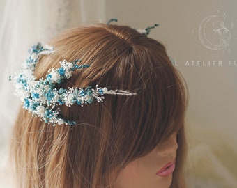 May include: A white and blue floral hairpiece with delicate sprigs and small flowers. The hairpiece is worn in a woman's hair.
