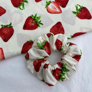 Może przedstawiać: Biała scrunchie z nadrukiem truskawek. Scrunchie jest wykonana z miękkiej, elastycznej tkaniny i ma marszczony design.