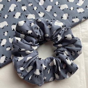 Puede incluir: Un scrunchie azul con un patr&oacute;n de ovejas blancas. El scrunchie est&aacute; hecho de tela y est&aacute; reunido en un c&iacute;rculo.