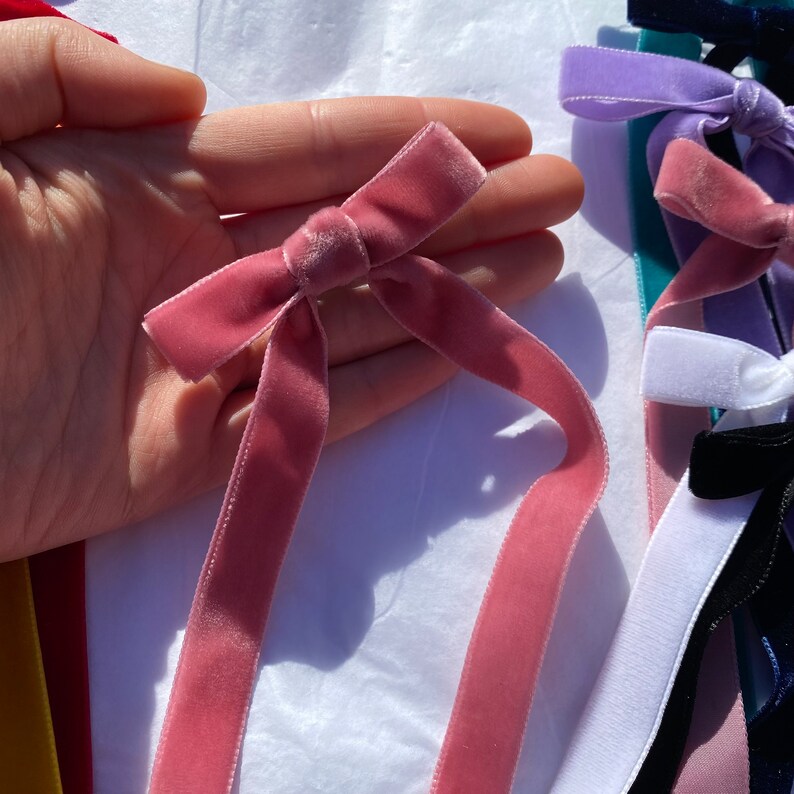 May include: A pink velvet ribbon tied into a bow. The ribbon is approximately 3.8 cm wide and is a soft, dusty pink colour.