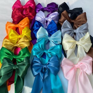 May include: A collection of colorful satin bows in various shades, including red, orange, yellow, green, blue, purple, and pink. The bows have long, flowing ribbons and are arranged closely together. The satin material gives them a shiny, elegant appearance.