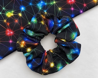Könnte beinhalten: Ein Haargummi aus Stoff mit schwarzem Hintergrund und einem lebendigen, mehrfarbigen Netzwerkmuster aus miteinander verbundenen Linien und leuchtenden Lichtpunkten in Rot, Gelb, Grün und Blau, das an eine digitale Konstellation oder Sternenkarte erinnert.