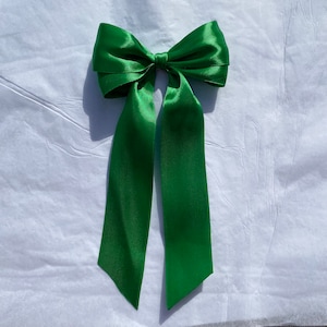 Peut inclure: Un grand nœud en satin vert avec de longues queues. Le nœud est noué dans un style classique avec les queues qui pendent.