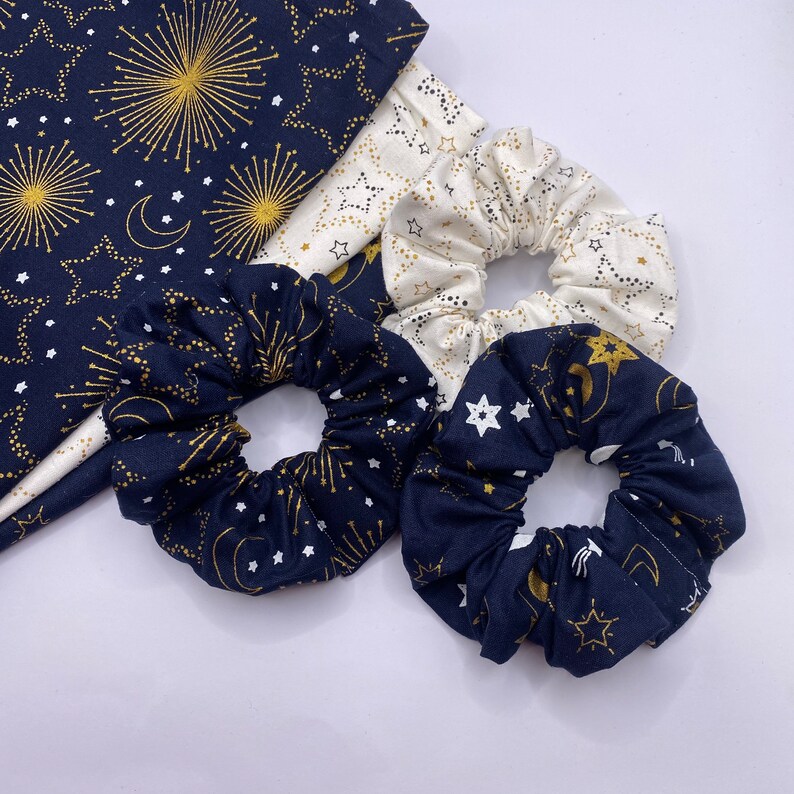 Puede incluir: Tres scrunchies para el pelo con un patr&oacute;n de estrellas y medias lunas azul marino y blanco. Los scrunchies est&aacute;n hechos de tela suave y son perfectos para a&ntilde;adir un toque de estilo a cualquier atuendo.