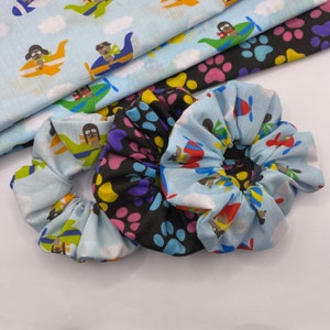 May include: Three colorful scrunchies with a paw print and airplane pattern. The scrunchies are made of soft fabric and are perfect for holding hair in place.
