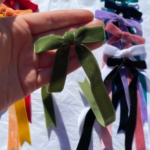 May include: A collection of velvet ribbon bows in various colors, including green, pink, blue, and yellow. The bows are tied with a simple knot and have long tails.