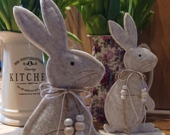Cute felt bunny perched upon a natural wooden base with a beaded double bow in neutral colours