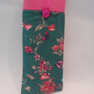 May include: A rectangular eyeglasses case with a teal floral pattern featuring pink flowers and butterflies. The top is a solid pink with a matching pink button closure and ribbon detail. The case is designed to protect eyewear.