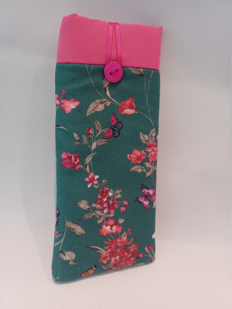 May include: A rectangular eyeglasses case with a teal floral pattern featuring pink flowers and butterflies. The top is a solid pink with a matching pink button closure and ribbon detail. The case is designed to protect eyewear.