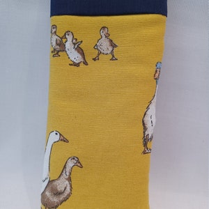 May include: A rectangular glasses case with a yellow background and a navy blue top. The case features a repeating pattern of ducks and geese in various poses. The case is made of fabric.