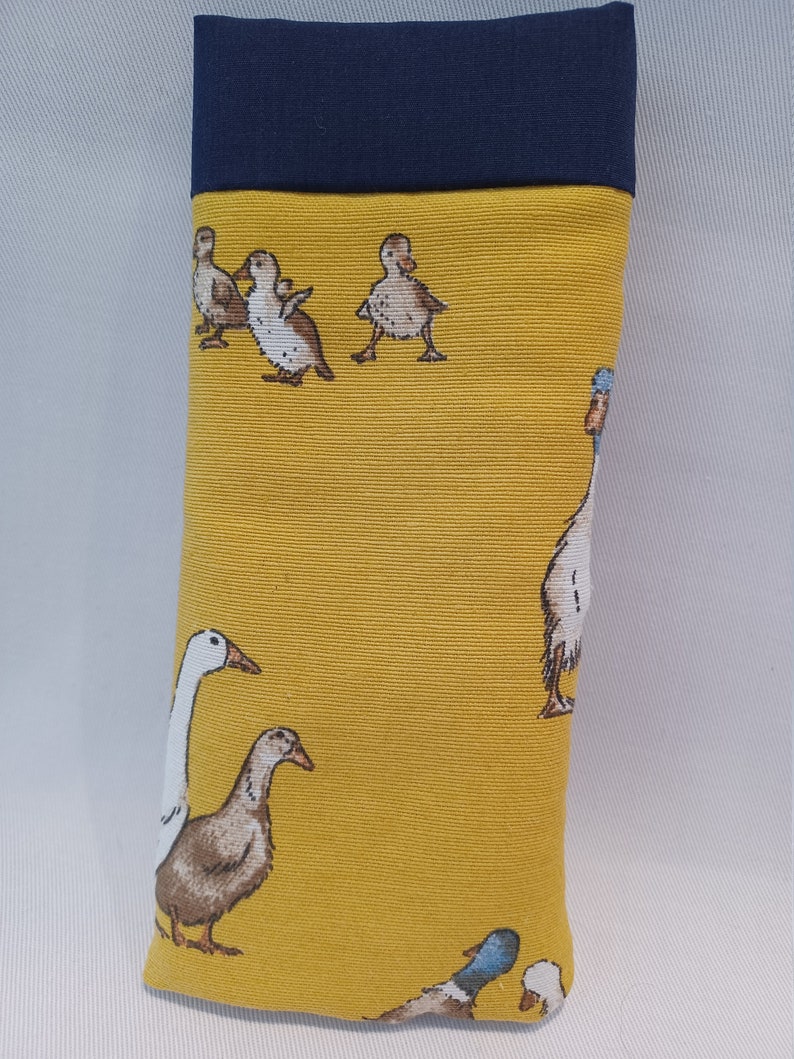 May include: A rectangular glasses case with a yellow background and a navy blue top. The case features a repeating pattern of ducks and geese in various poses. The case is made of fabric.