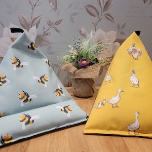 May include: Two triangular reading pillows, one with a blue background and a bee pattern, the other with a yellow background and a duck pattern.