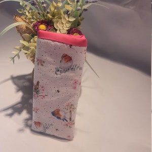 May include: A fabric glasses case with a pink trim and a bird and floral pattern. The case is white with small black dots and features illustrations of birds, flowers, and butterflies. The case is folded and stands upright.