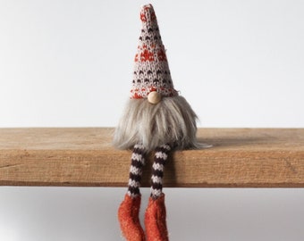 A charming knitted sitting Gonk decoration dressed in Autumnal clothes in a rich burnt orange hues with cute wooden nose