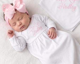 May include: A white long-sleeve baby gown with a pink embroidered bow and the name Hadley, paired with a matching pink bow headband and a white blanket featuring the same pink bow and name Hadley embroidered in the corner.