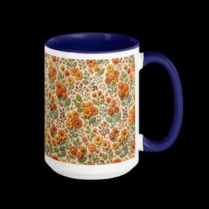 Puede incluir: Taza de cerámica blanca con asa e interior azul marino. La taza presenta un patrón repetido de flores naranjas y amarillas con hojas verdes. Las flores están sobre un fondo color crema.