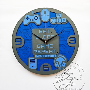 Pode incluir: Um relógio de parede redondo com tema de jogos, em azul e cinza. Apresenta um design de placa de circuito, com ícones de jogos como um controlador, um rato e auscultadores. O texto "EAT. SLEEP. GAME. REPEAT. PLAYER: MARTIN" é exibido.