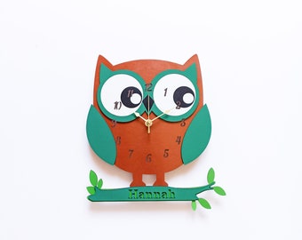 May include: A brown and green owl-shaped clock with black hands and white eyes. The clock is on a branch with green leaves and the name "Hannah" is written on the branch.