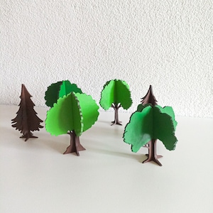 May include: Five wooden cutout trees, four with green leaves and one with brown branches. The trees are on a white surface.