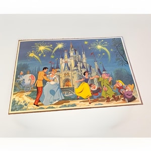 May include: A rectangular print featuring a nighttime scene with a large castle, yellow fireworks, and Disney characters. Cinderella and Prince Charming dance on the left, while Snow White and several dwarfs celebrate on the right.