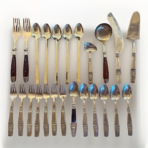 May include: An assortment of vintage silverware, including forks, spoons, and serving utensils. The forks have dark brown handles, while the spoons and serving pieces are gold-toned. The set includes a cake server and a ladle.