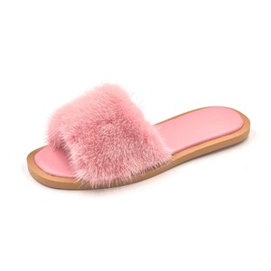 May include: A single pink faux fur slide sandal. The sandal features a fluffy, textured strap and a smooth, light pink footbed. The sole is a light brown color.