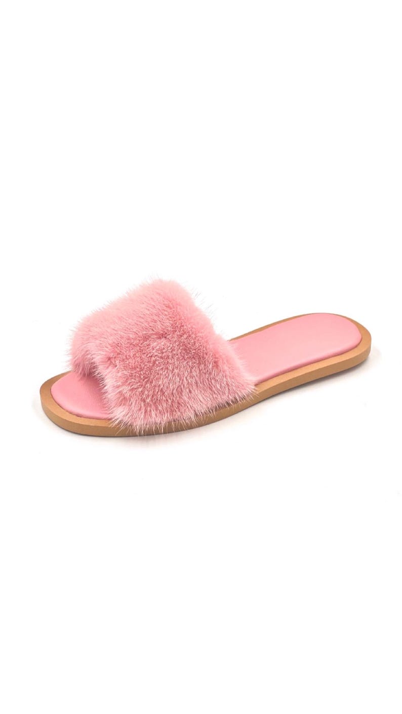 May include: A single pink faux fur slide sandal. The sandal features a fluffy, textured strap and a smooth, light pink footbed. The sole is a light brown color.