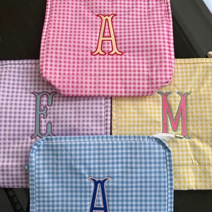 Könnte beinhalten: Fünf quadratische Täschchen mit Vichy-Muster in Rosa, Lavendel, Gelb und Blau. Jedes Täschchen hat einen gestickten Buchstaben: A, E, M und A. Die Täschchen dienen wahrscheinlich zur Aufbewahrung.