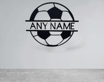 Può includere: Arte da parete a forma di pallone da calcio in metallo nero con la scritta "ANY NAME" intagliata al centro. Il design del pallone da calcio è un classico motivo a pentagoni ed esagoni. L'opera è montata su una parete bianca.