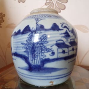 May include: A blue and white ceramic jar with a landscape design. The jar has a round body and a wide mouth.