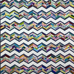 Pode incluir: Uma colcha colorida com um padrão chevron feito de vários pedaços de tecido. A colcha é branca com linhas cinzas e apresenta uma variedade de cores e padrões no design chevron.