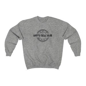 May include: A heather gray sweatshirt with a circular graphic featuring Roman numerals and the text "HAPPY NEW YEAR" in black. The sweatshirt has a crew neck and long sleeves.