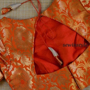 May include: A red brocade blouse with a gold floral pattern and a low back with a tie closure. The blouse has a  "sewinstyle" watermark.