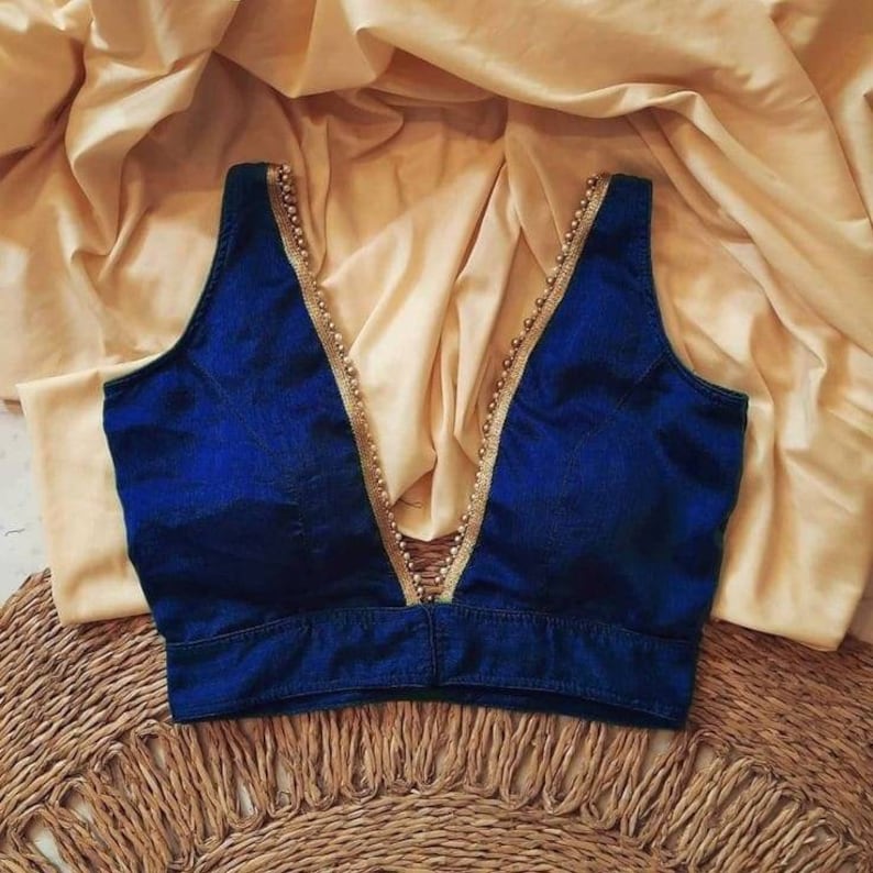 Peut inclure: Un chemisier bleu fonc&eacute; sans manches avec un d&eacute;collet&eacute; plongeant. Le d&eacute;collet&eacute; est orn&eacute; d'une bordure de perles dor&eacute;es.