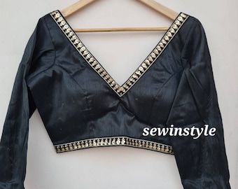 May include: A black silk blouse with a deep V-neckline and gold trim. The trim features a repeating pattern of small, gold flowers. The blouse has long sleeves and a fitted silhouette. The text "sewinstyle" is visible in the lower right corner of the image.